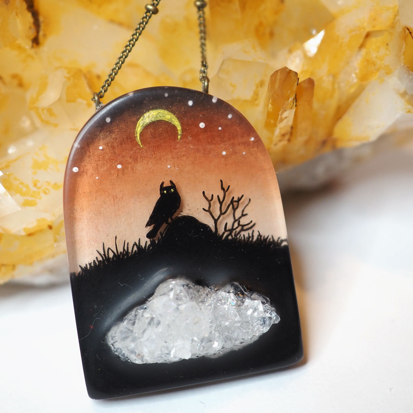 A hand-painted resin pendant featuring a night scene with an owl under a crescent moon with an imbedded druzy geode piece