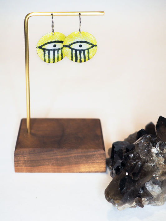 Dangle earrings featuring hand-painted yellow enamel eyes on hammered silver circles