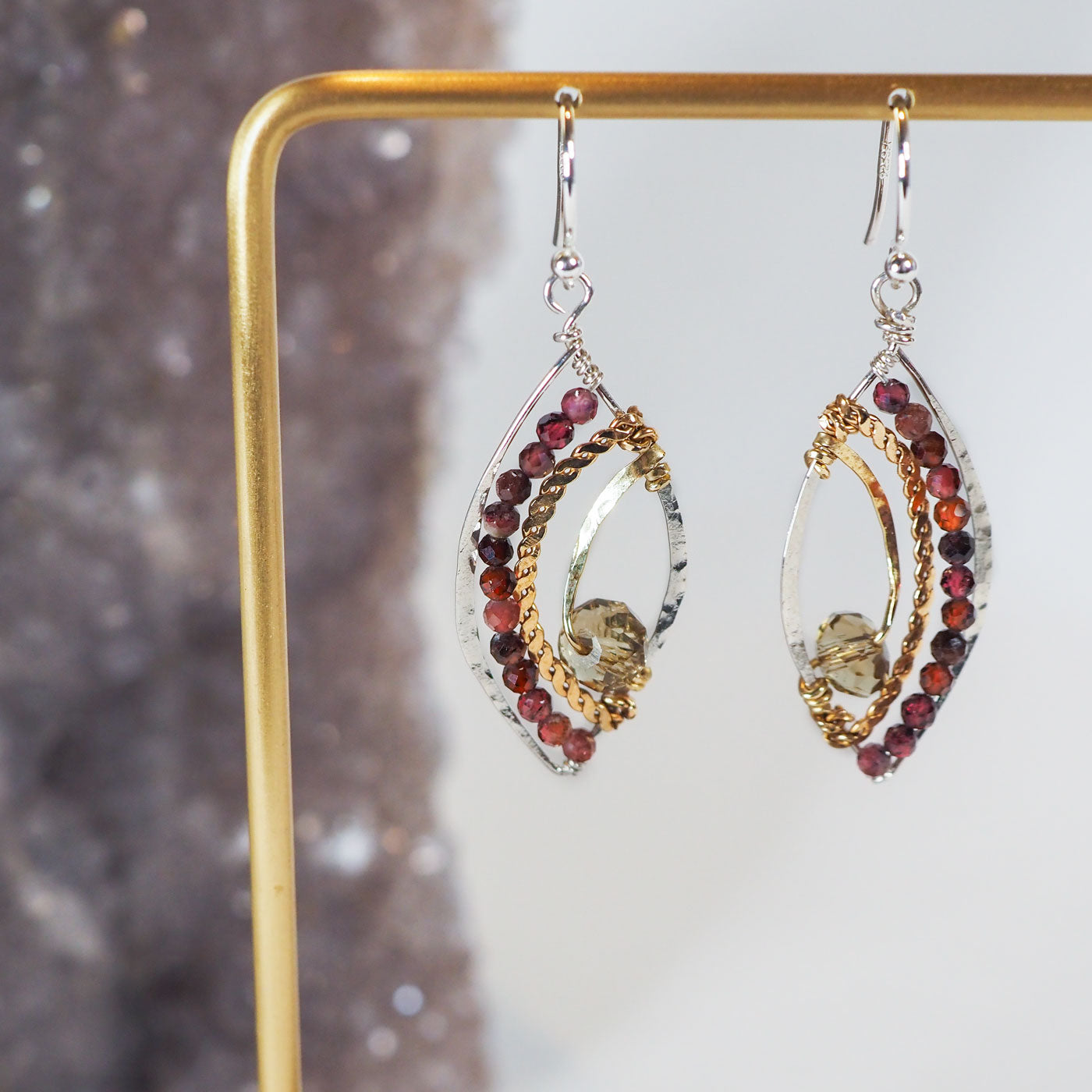 Faceted garnet gemstones lines the wings of these sterling silver earrings, accented by brass and crystal elements with a sterling silver french hook.