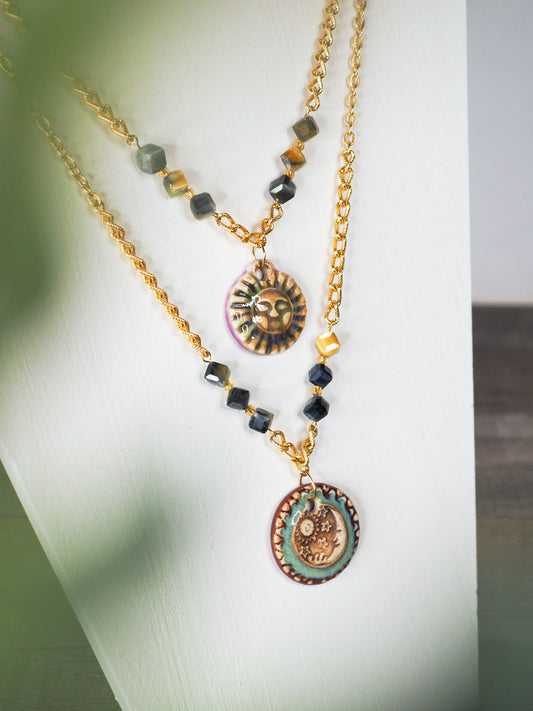 Hand-made ceramic sun and moon pendants hang between faceted blue Tiger's Eye beads on adjustable vintage gold chain necklaces.