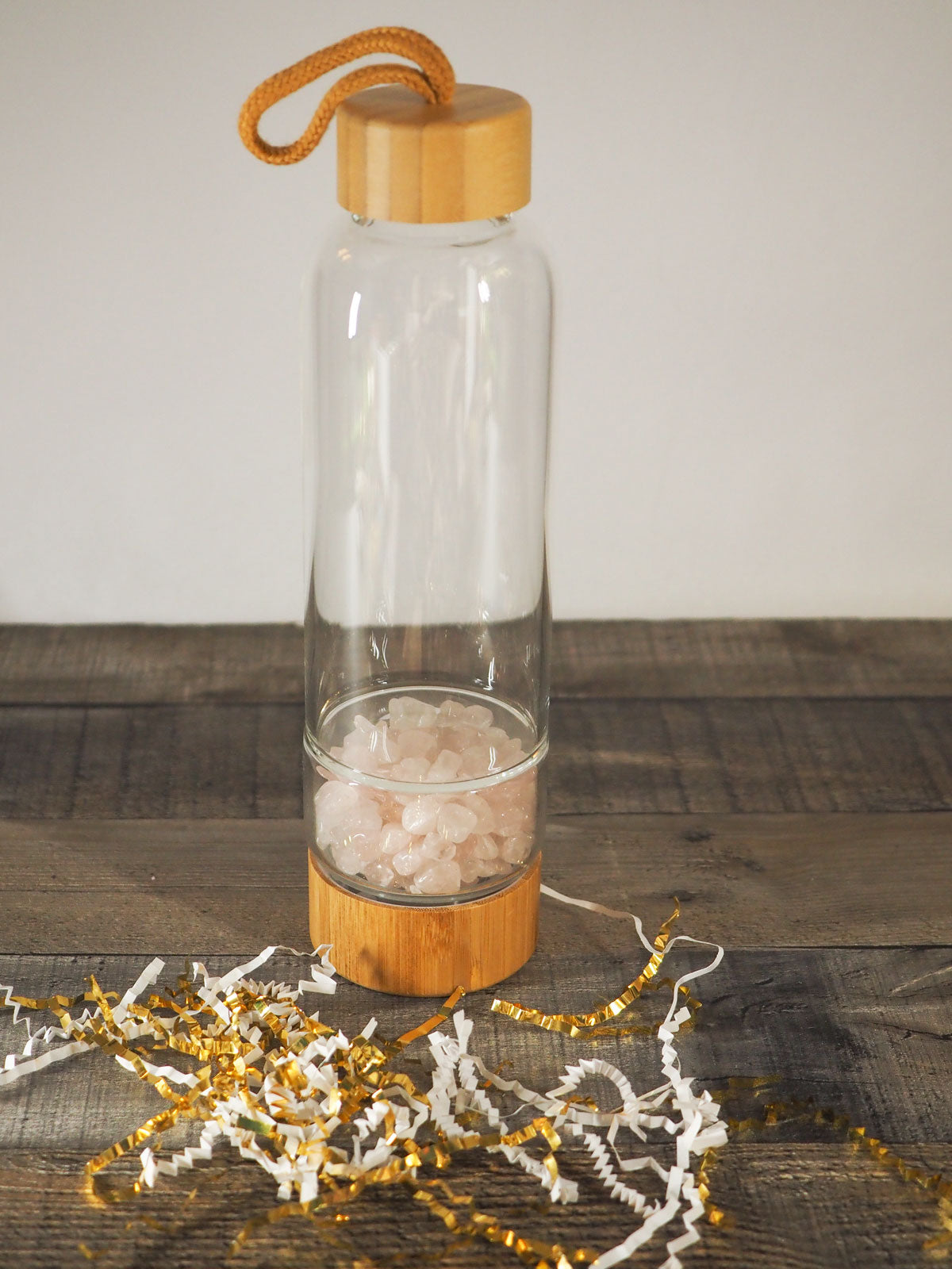 A bamboo and glass water bottle with tumbled rose quartz chips in the bottem