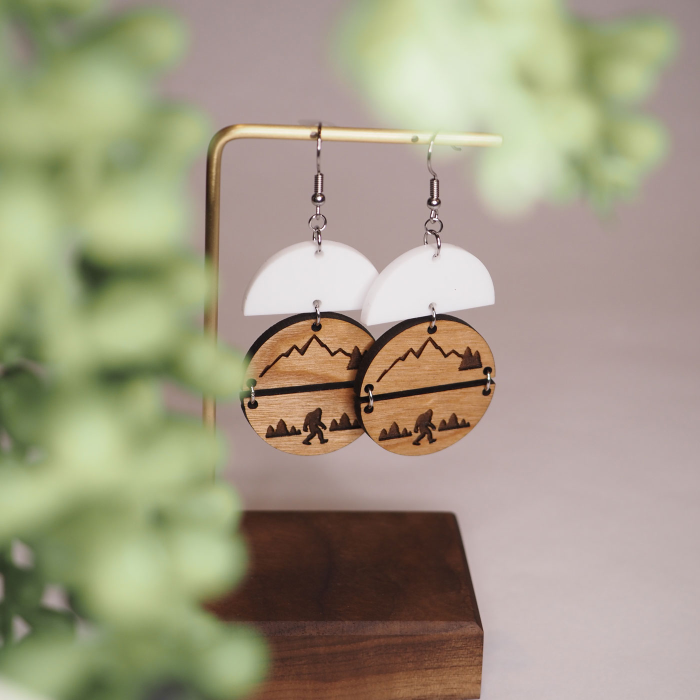 Cherry wood round earrings with bigfoot mountain scene hanging under white acrylic half circles