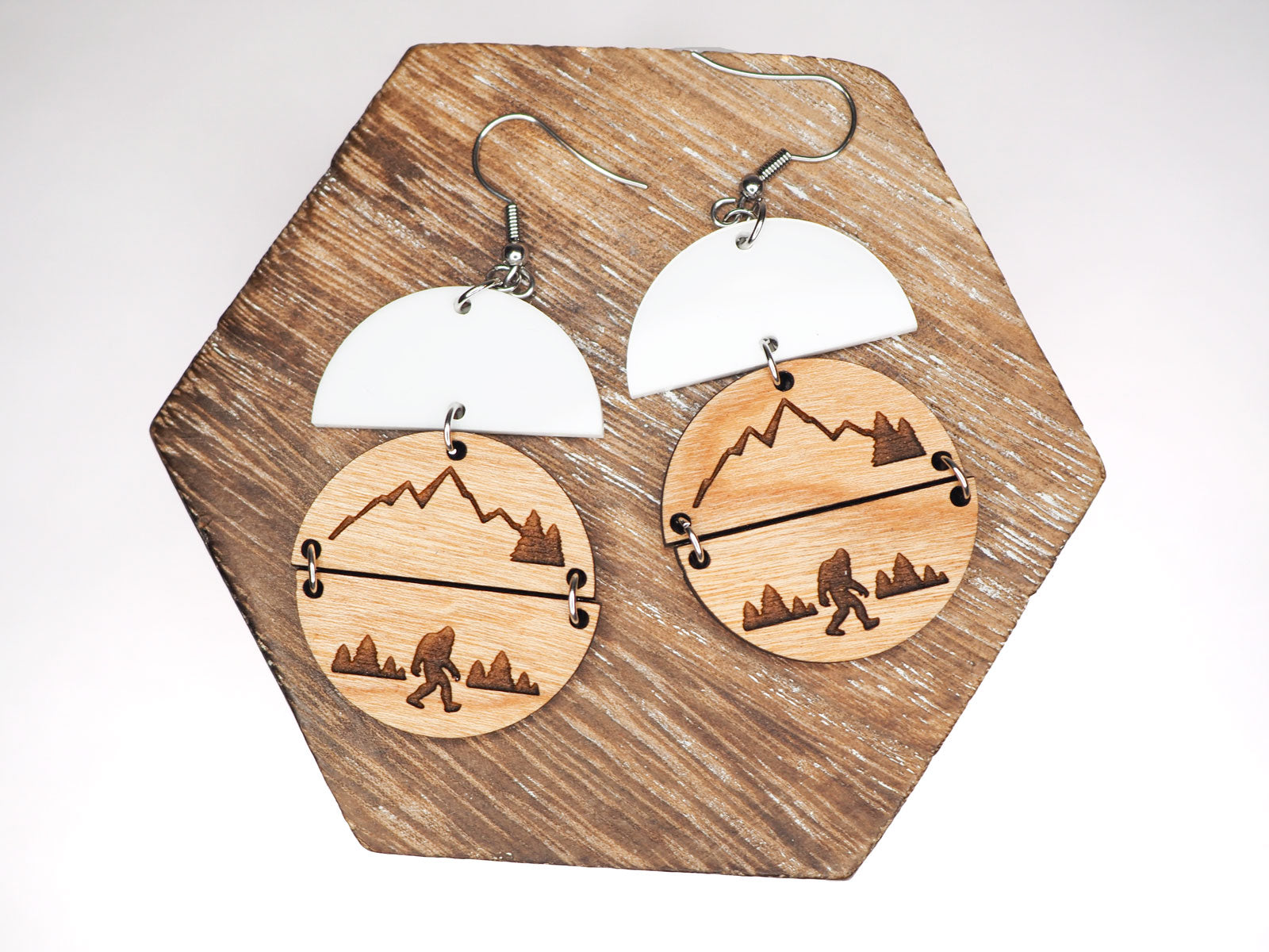 Cherry wood round earrings with bigfoot mountain scene hanging under white acrylic half circles
