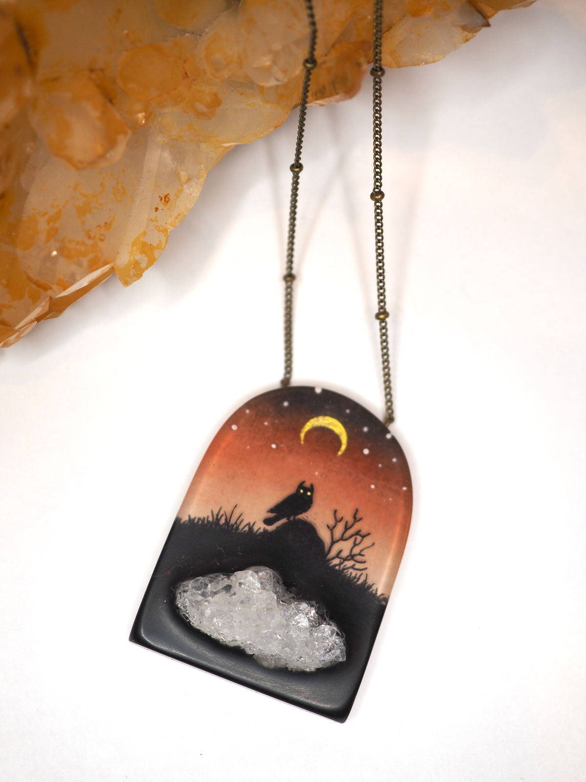 A hand-painted resin pendant featuring a night scene with an owl under a crescent moon with an imbedded druzy geode piece