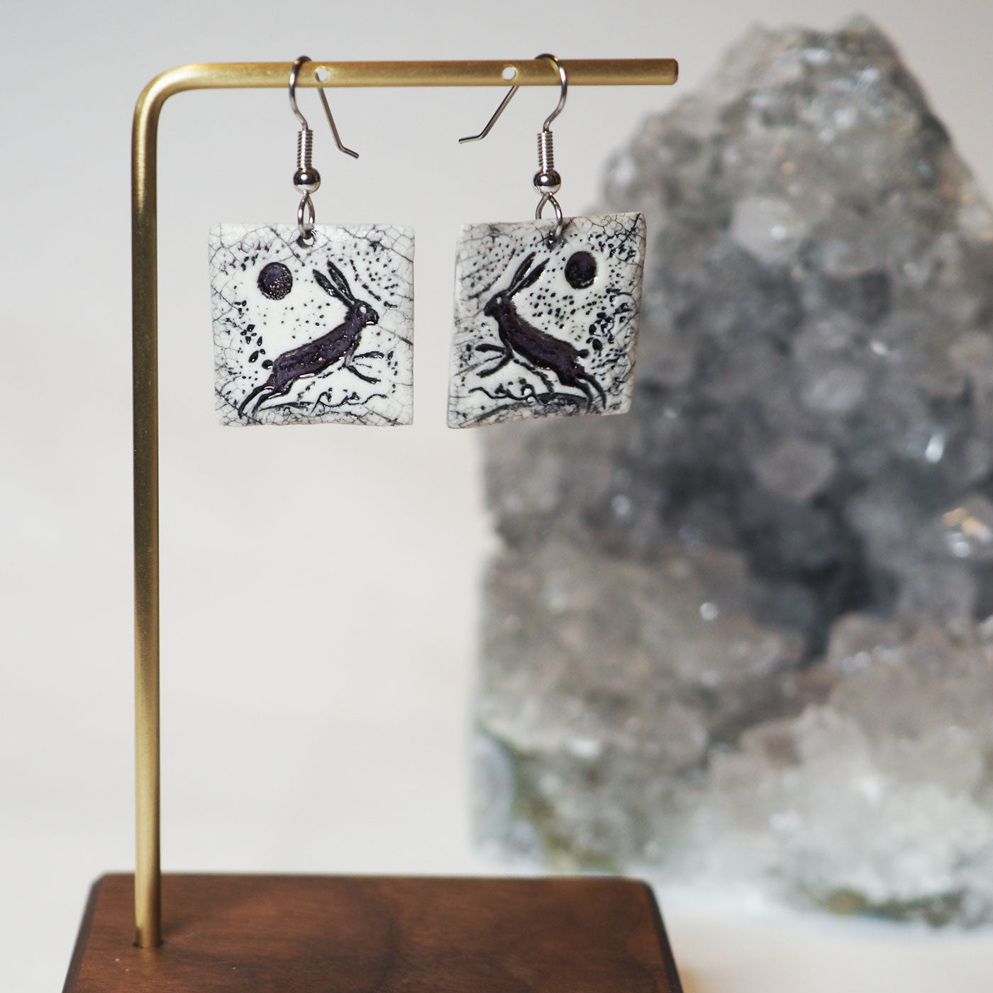 Black and white hand-made ceramic square dangle earrings featuring a scene of a wild rabbit running beneath a full moon
