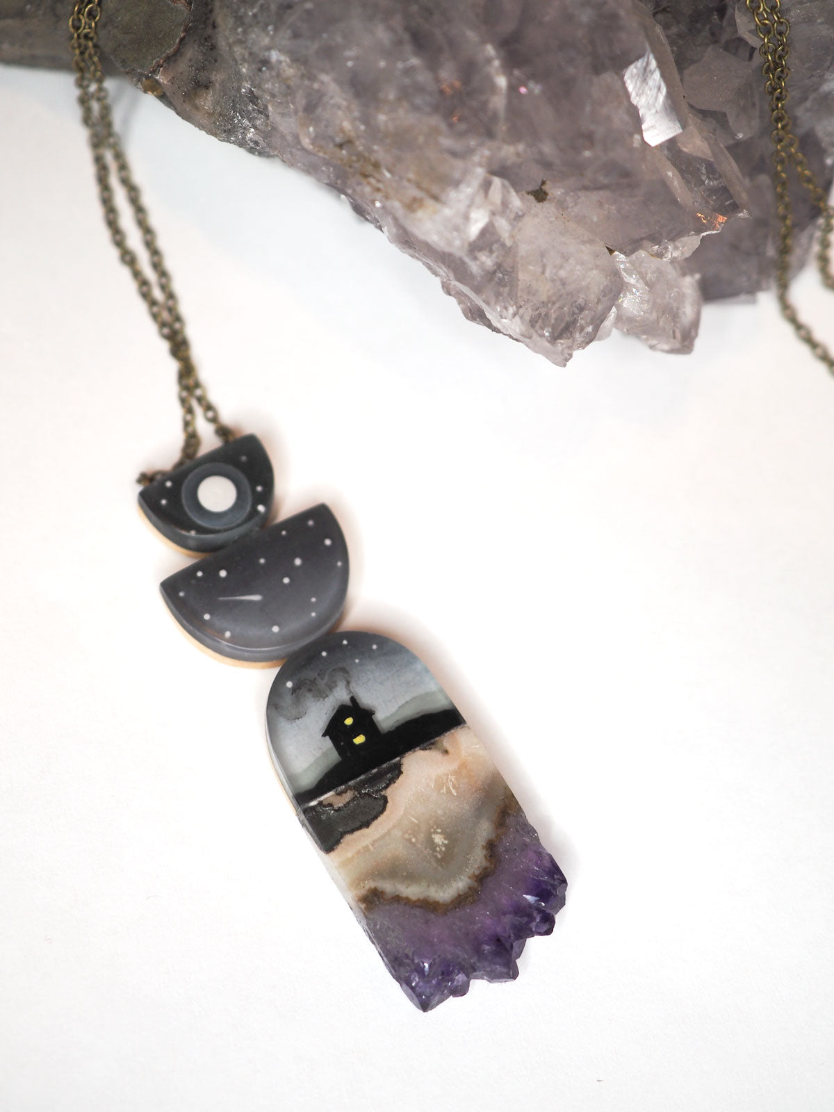 Hand-painted resin and amethyst slice necklace featuring 2 half circles on top of a silhouette of a house at night under a full moon and shooting stars