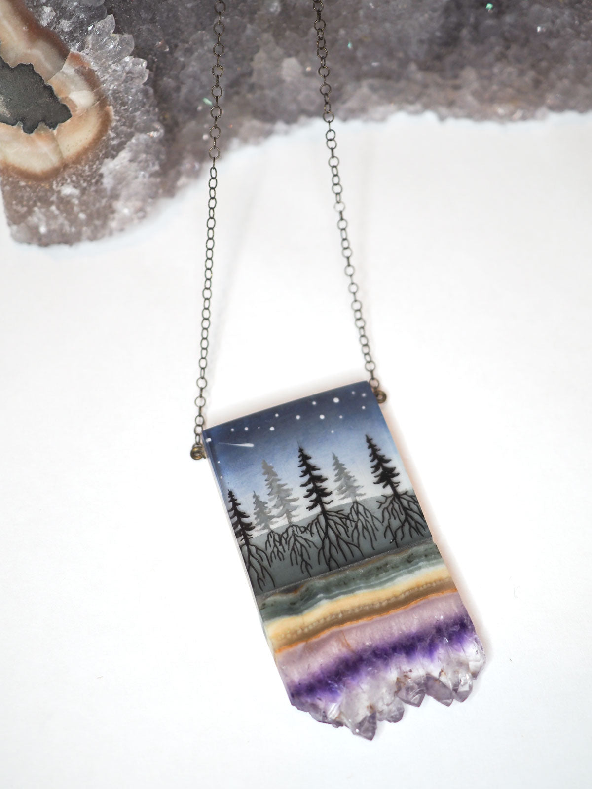Hand-painted resin and amethyst slice rectangular necklace featuring a scene of a forest with its roots going into the ground, under a night sky with shooting stars on a silver chain