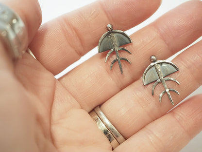 Small hand-made hammered silver post earrings in the shape of a stylized trilobite shown in a hand to show size