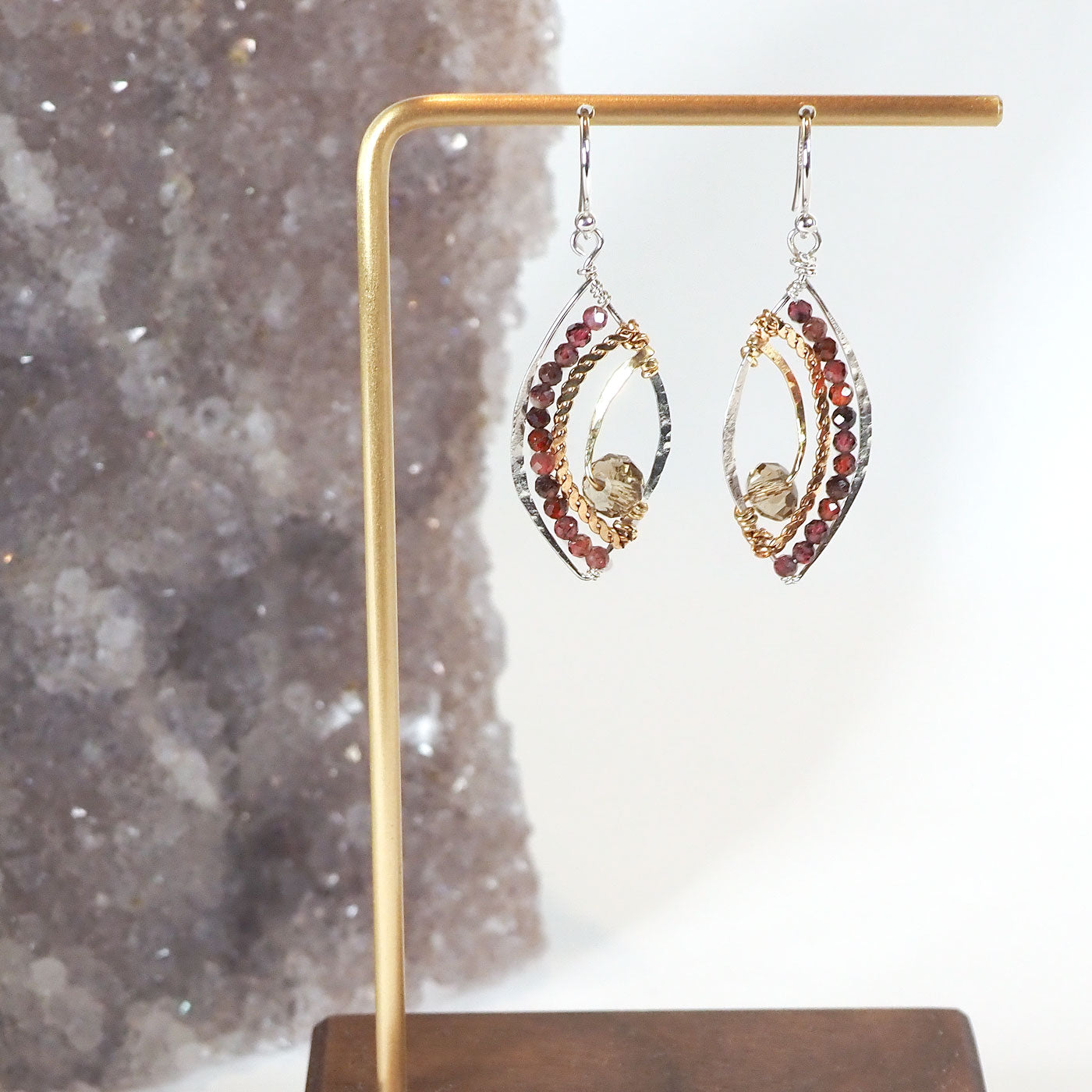 Faceted garnet gemstones lines the wings of these sterling silver earrings, accented by brass and crystal elements with a sterling silver french hook.