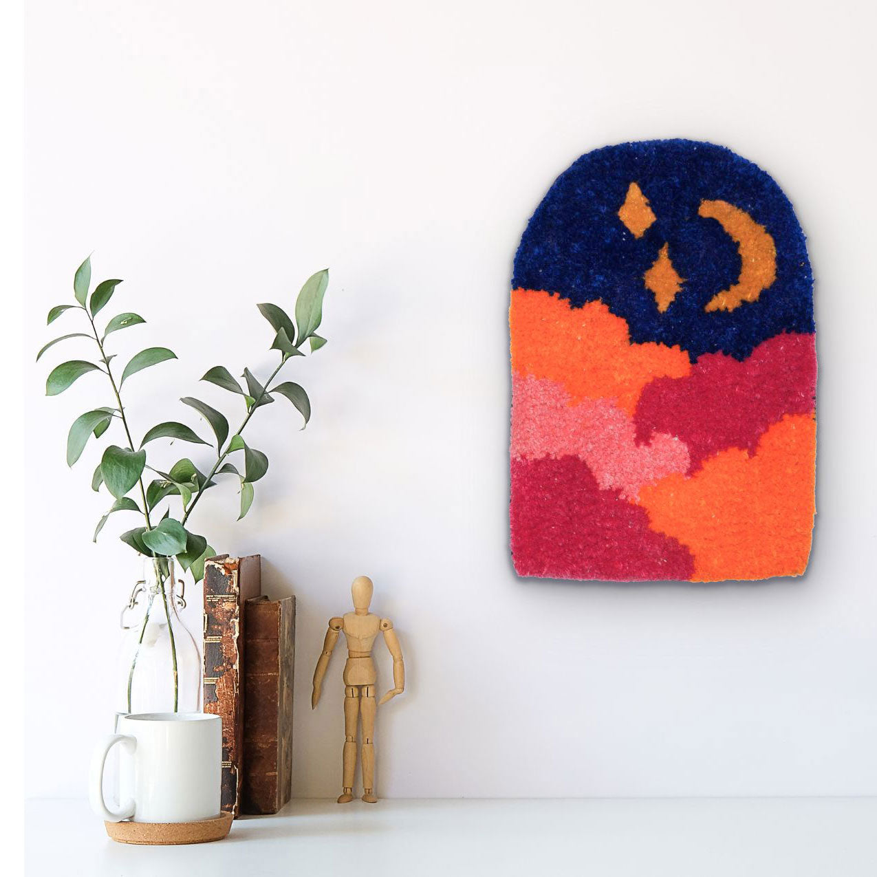 Hand-tufted wall hanging with a night scene of a crescent moon and stars above orange and pink clouds