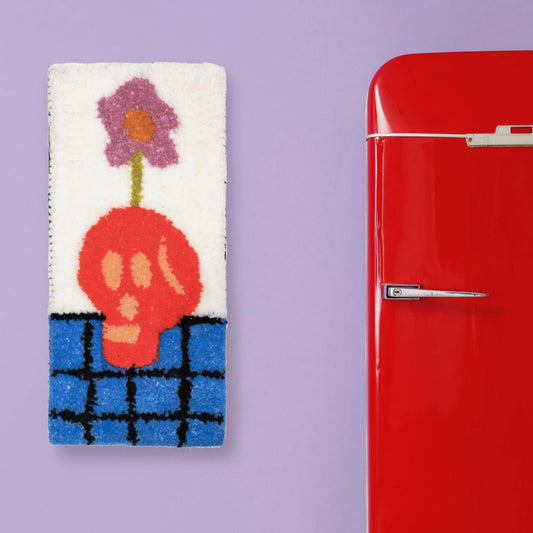 Hand-tufted wall hanging featuring a red skull on a blue checked surface with a purple flower coming out of the top of its head