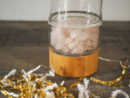 A bamboo and glass water bottle with tumbled rose quartz chips in the bottem