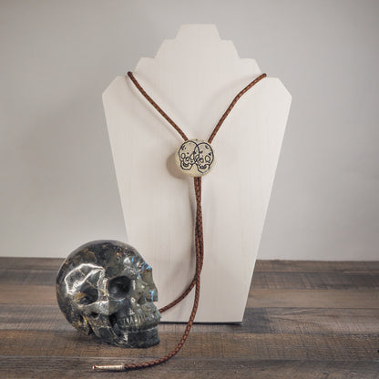Skull illustration is carved and hand-painted onto white stoneware pendant with cobalt blue inlay, bolo tie hung on leather cords - Shown with a labradorite crystal skull