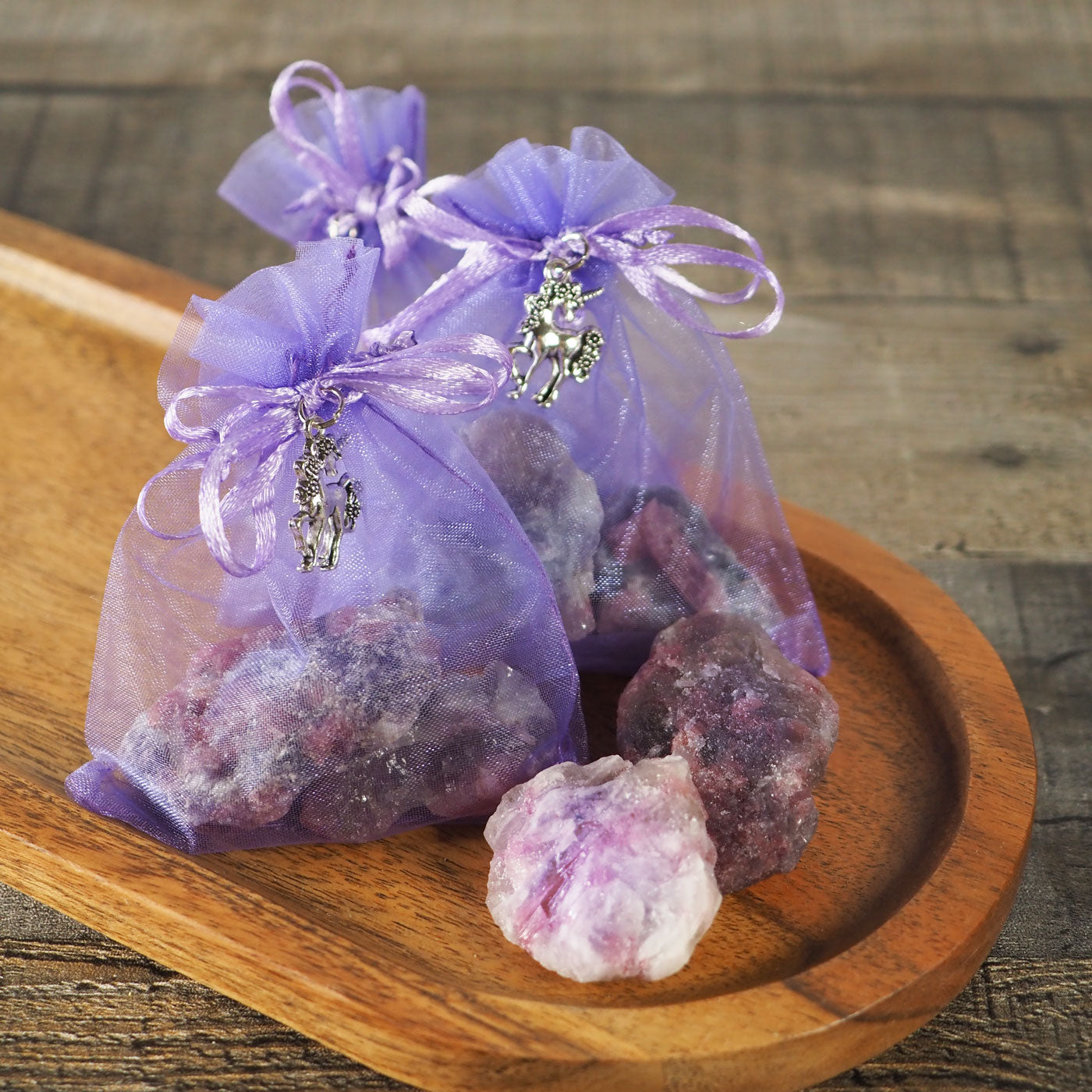 3 Small Purple Organza Sacks tied with a Unicorn Charm, each containing 2 Rough Unicorn Stones, Shown with 2 Rough Unicorn Stones beside them